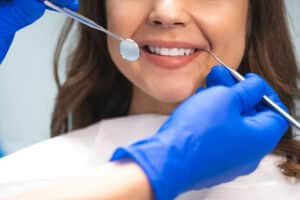 Smiling,Brunette,Woman,Patient,Examined,By,Dentist,In,Blue,Gloves