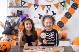 Two young girls in Halloween costumes smiling and holding up cookies